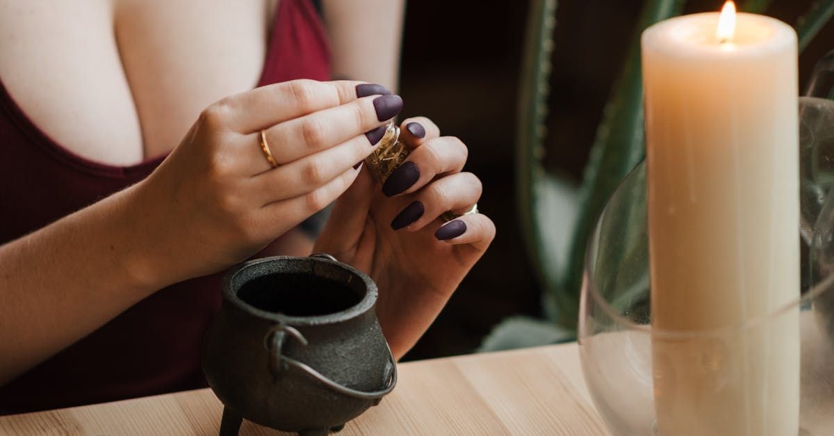 A woman is sitting at a table with a candle and a cauldron.