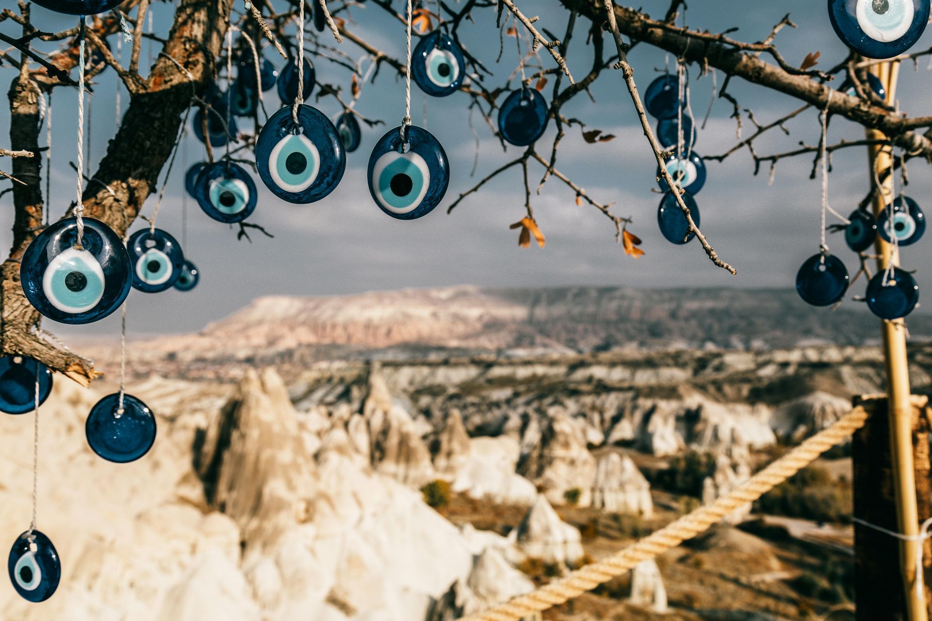 Blue evil eye charms hanging on a tree branch, with a scenic mountain landscape in the blurred background.