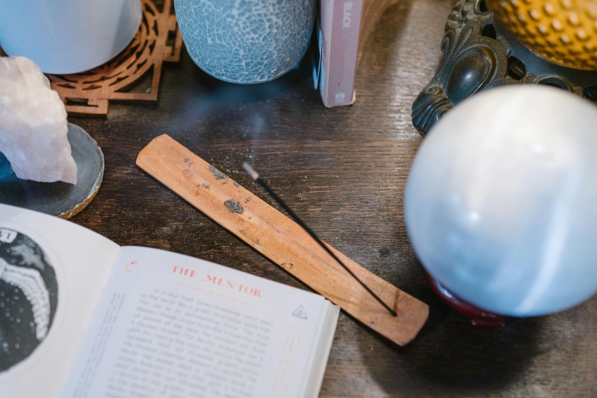 A wooden incense burner is sitting on a table next to a book and a crystal ball.