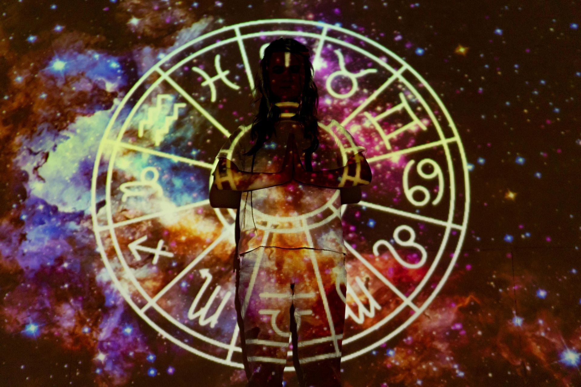 Person silhouetted with the zodiac wheel projected on them against a galaxy backdrop.