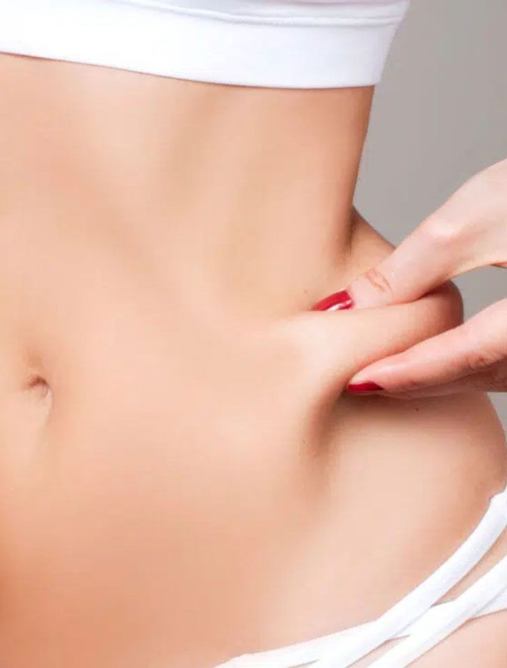 A woman is pinching her stomach with her fingers.