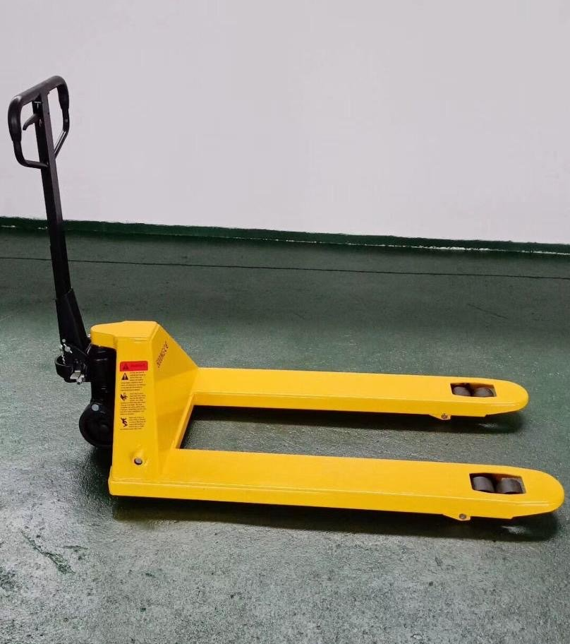 Una transpaleta amarilla está parada sobre un suelo verde.