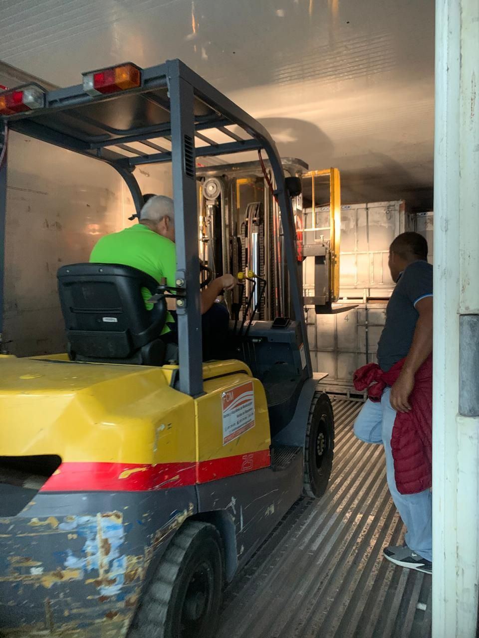 Un hombre con una camisa verde conduce una carretilla elevadora amarilla.