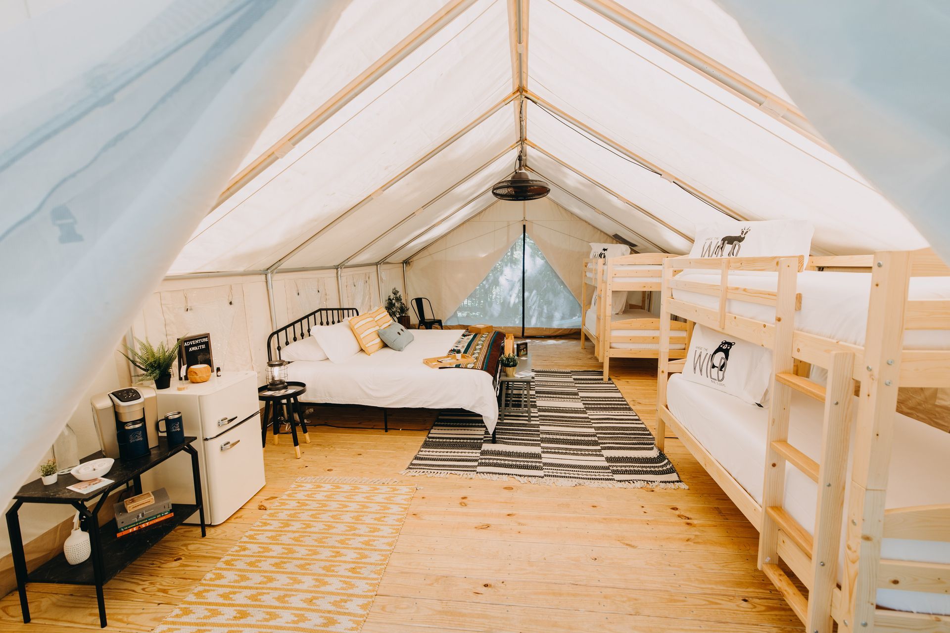 Interior of a glamping tent with beds, a rug, a small fridge, and a coffee setup.