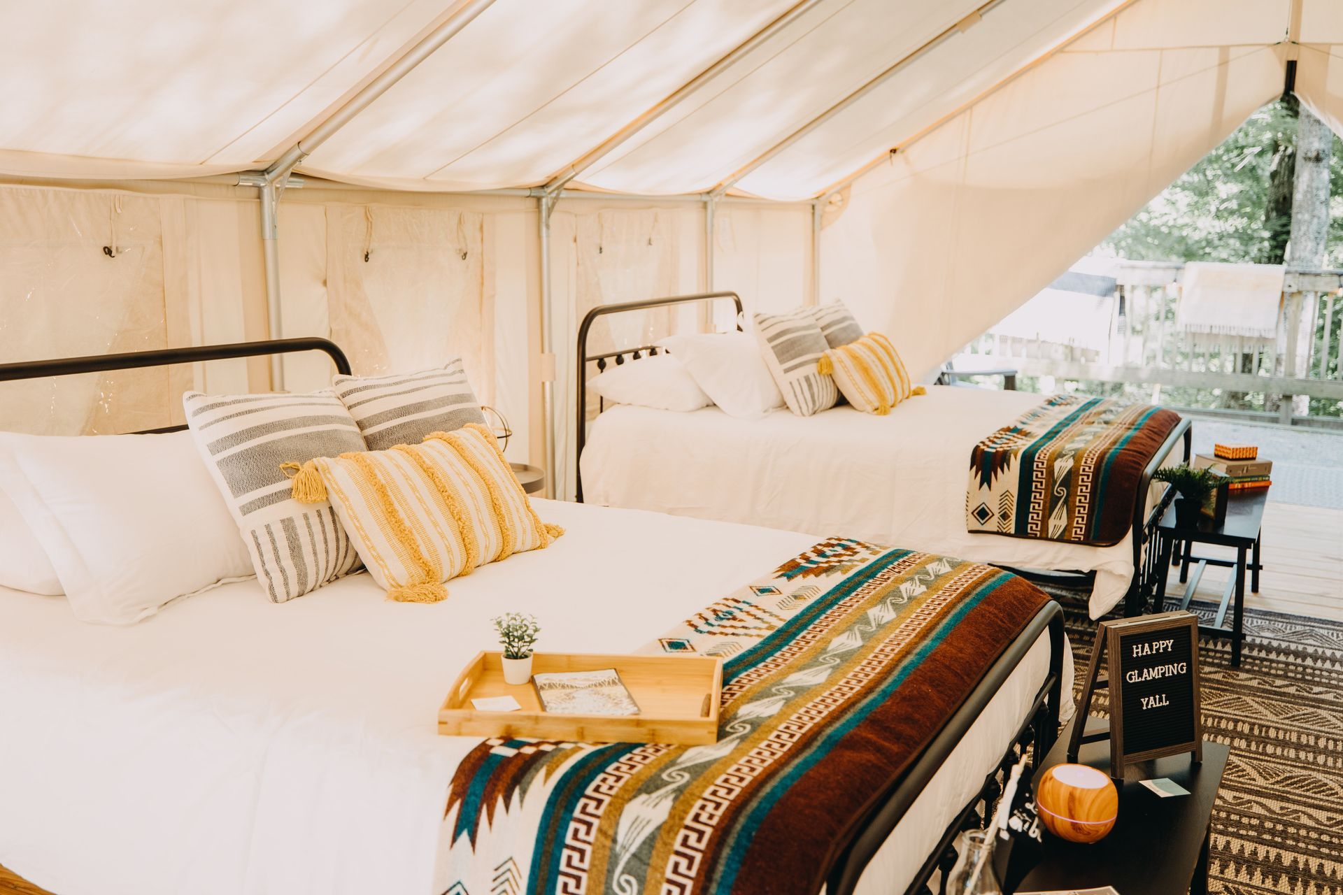Two beds inside a canvas tent, with decorative pillows and blankets.