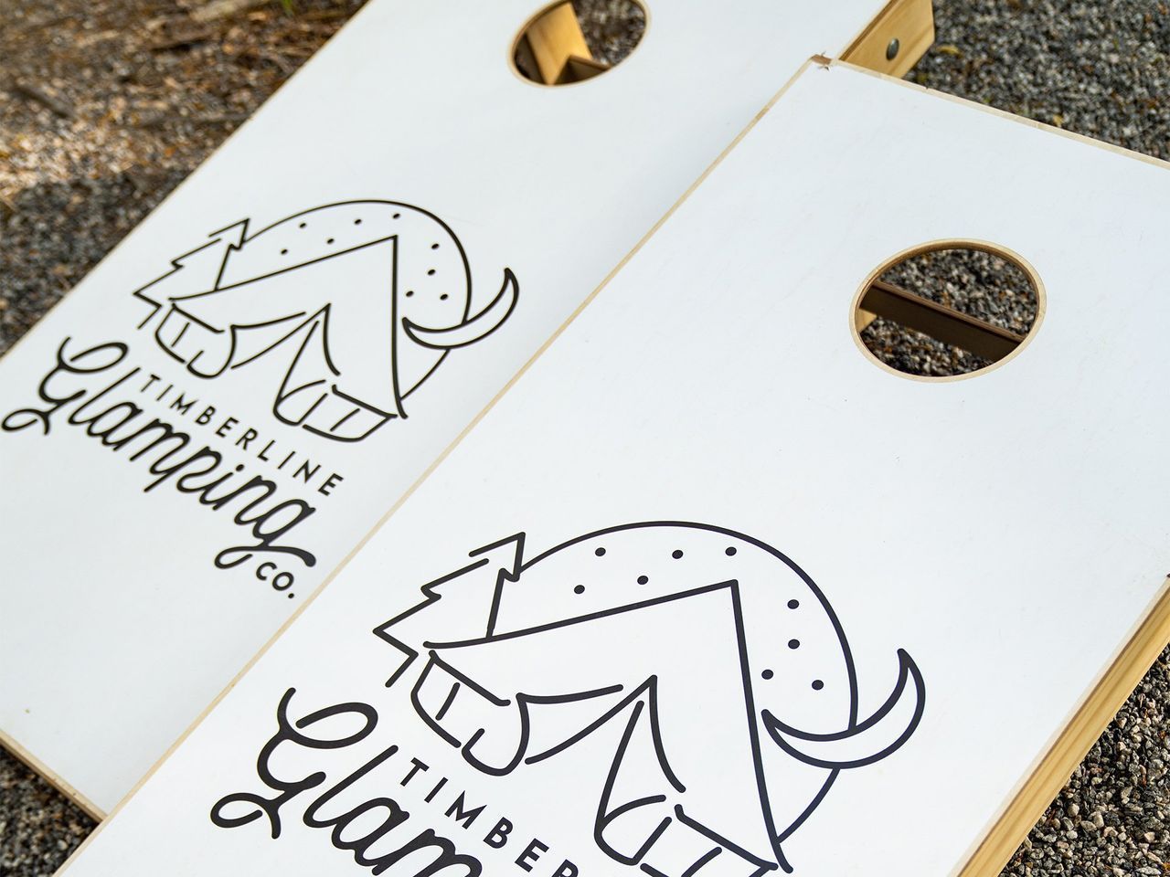 Two white cornhole boards with a black logo for
