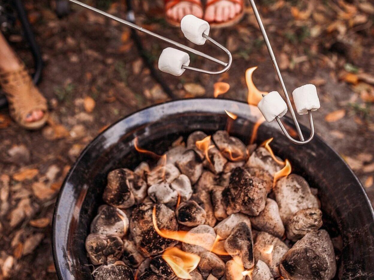 Marshmallows roasting over charcoal fire in a black fire pit.