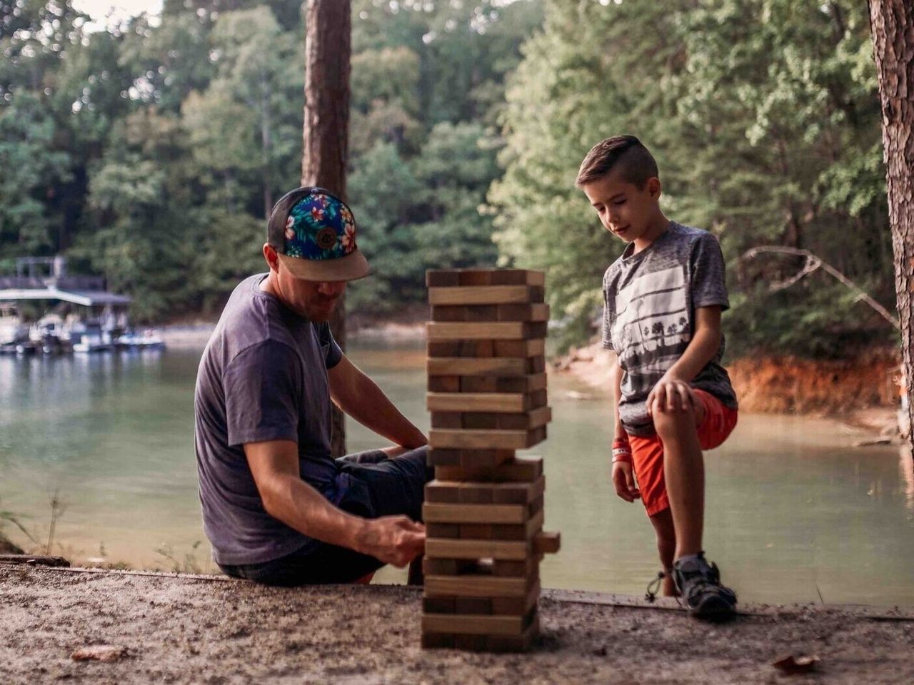 Man and child playing Jenga by a lake.
