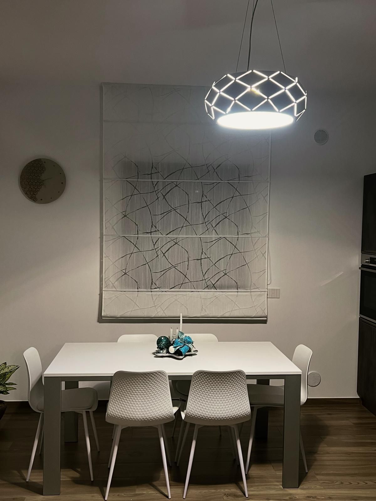Sala da pranzo con tavolo bianco, sedie, quadri e una lampada decorativa.