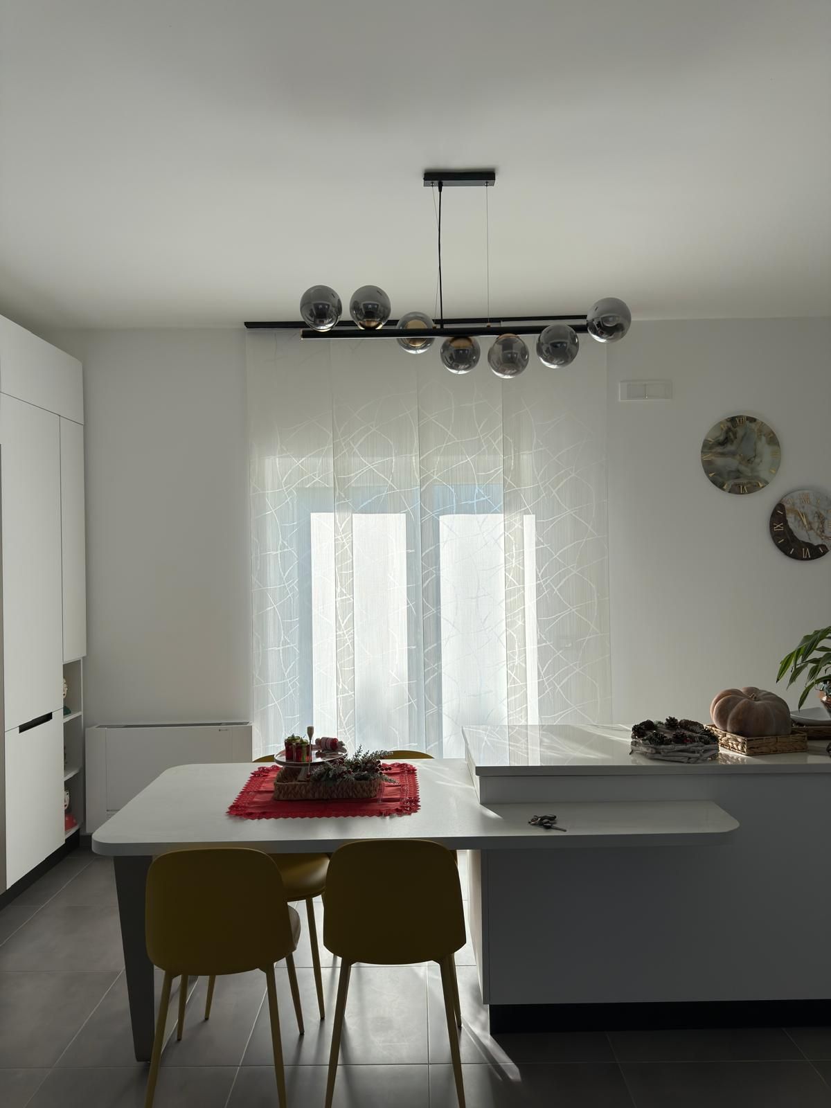 Sala da pranzo con tavolo bianco, sedie gialle e lampadario moderno.