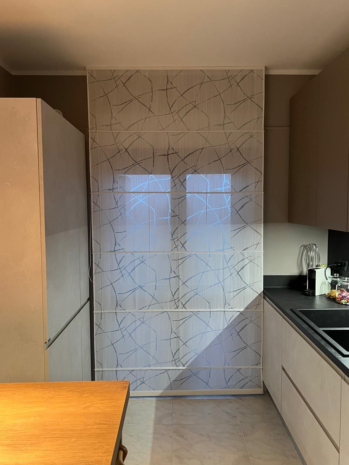 Cucina con mobili bianchi, parete decorativa, due finestre e piano di lavoro scuro.