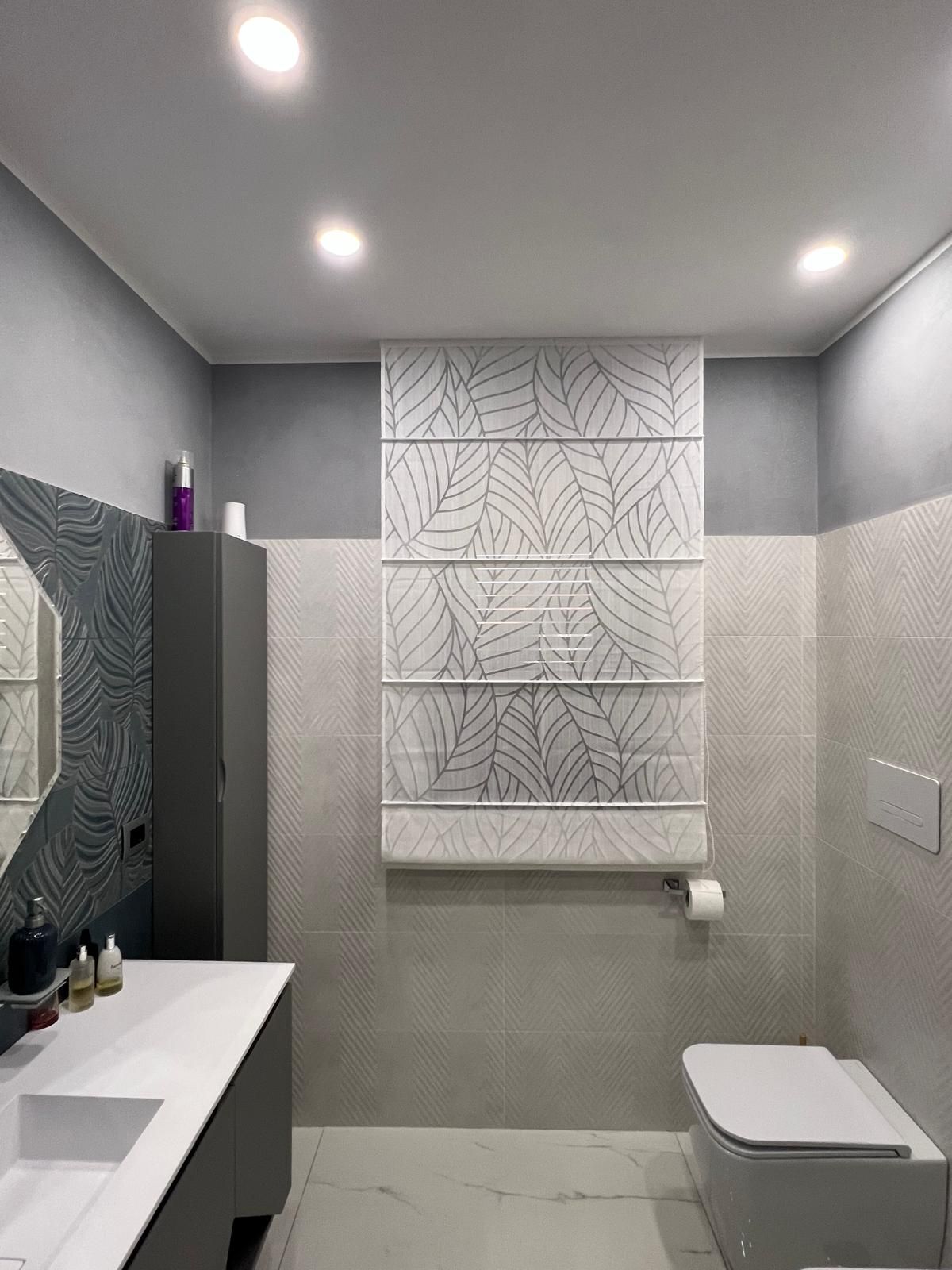 Bagno moderno con pareti grigie, sanitari bianchi e tenda romana con motivi.