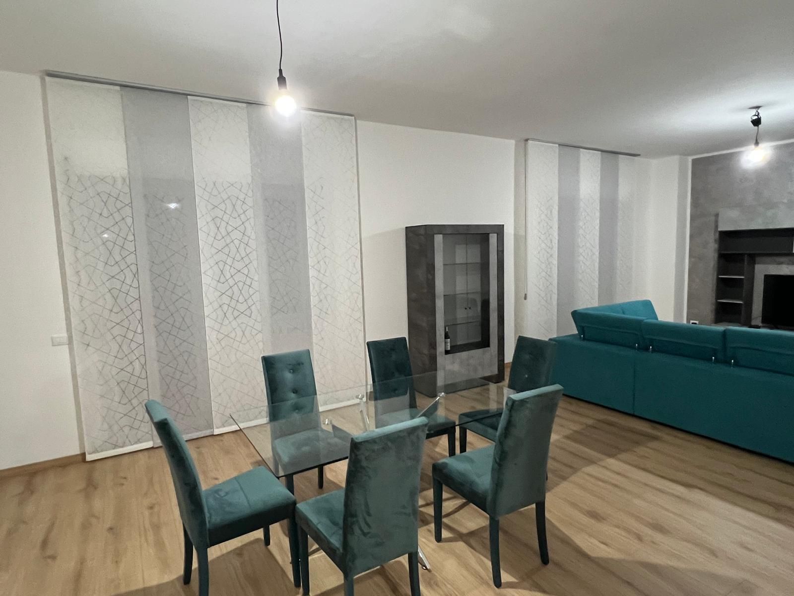 Zona pranzo con tavolo in vetro, sedie color verde acqua, tende a fantasia e divano color verde acqua.