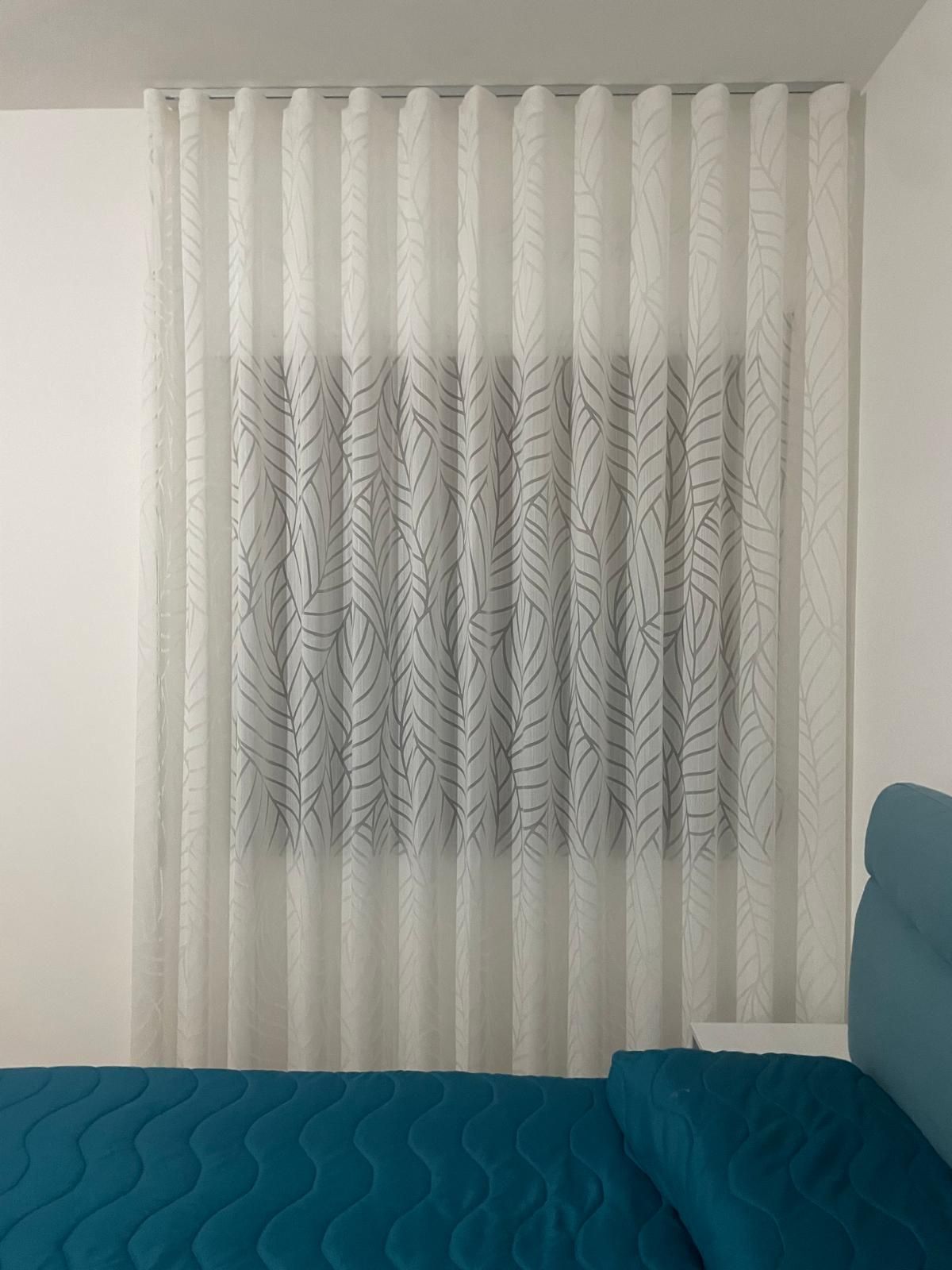 Tende bianche e trasparenti sopra una finestra, sopra un letto turchese.