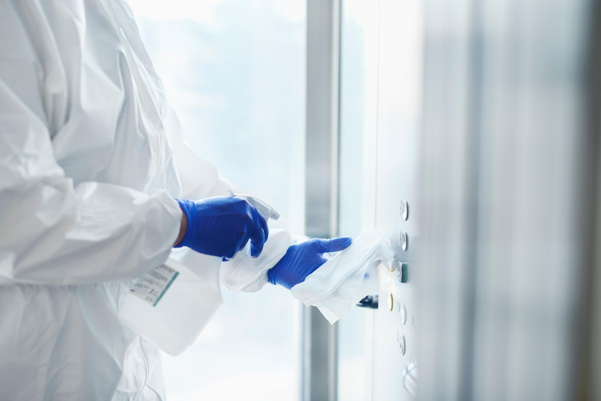 Person in protective suit sanitizing a door handle with spray and wipe.