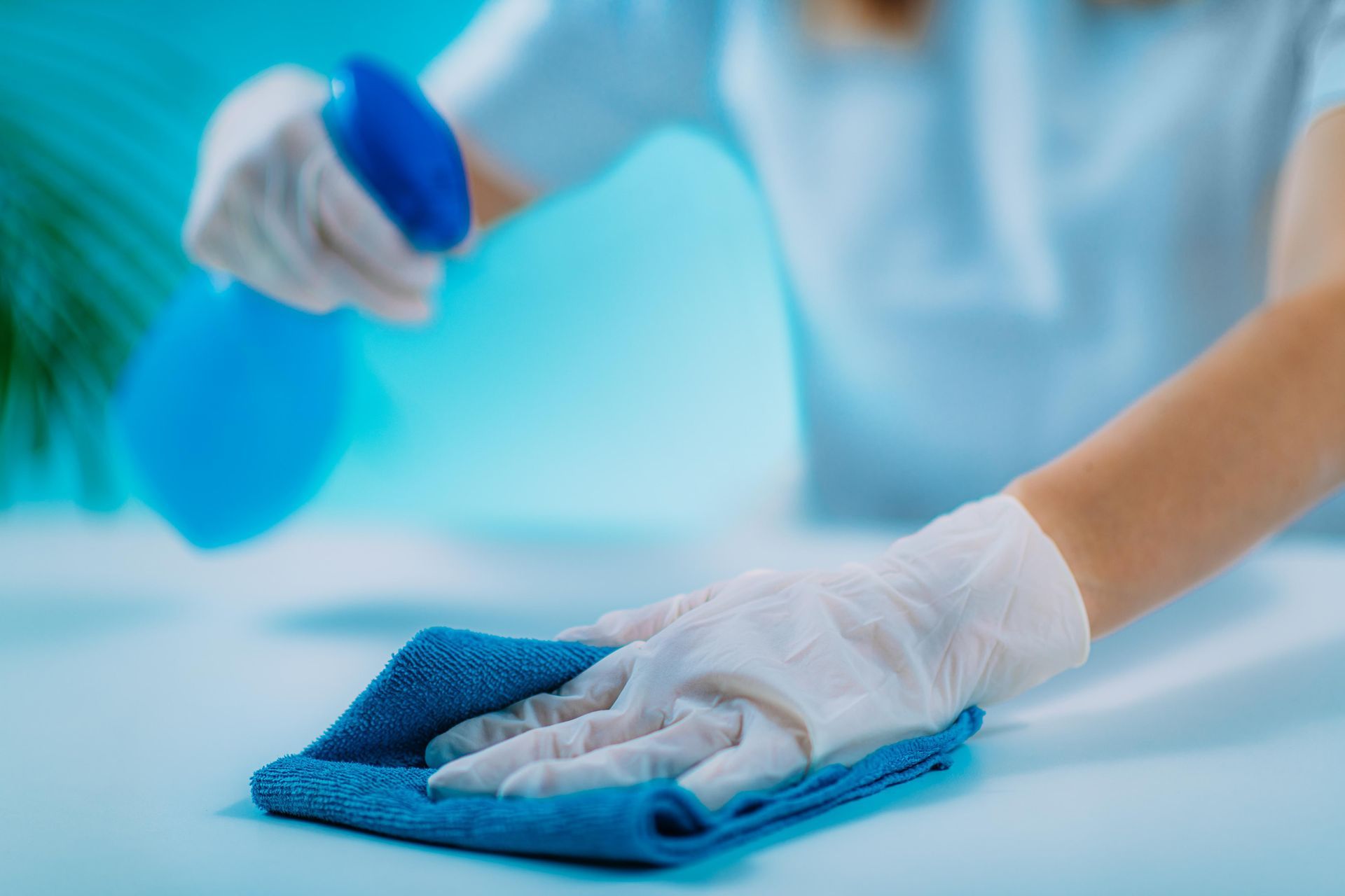Person wearing gloves spraying and wiping a blue surface with a microfiber cloth.