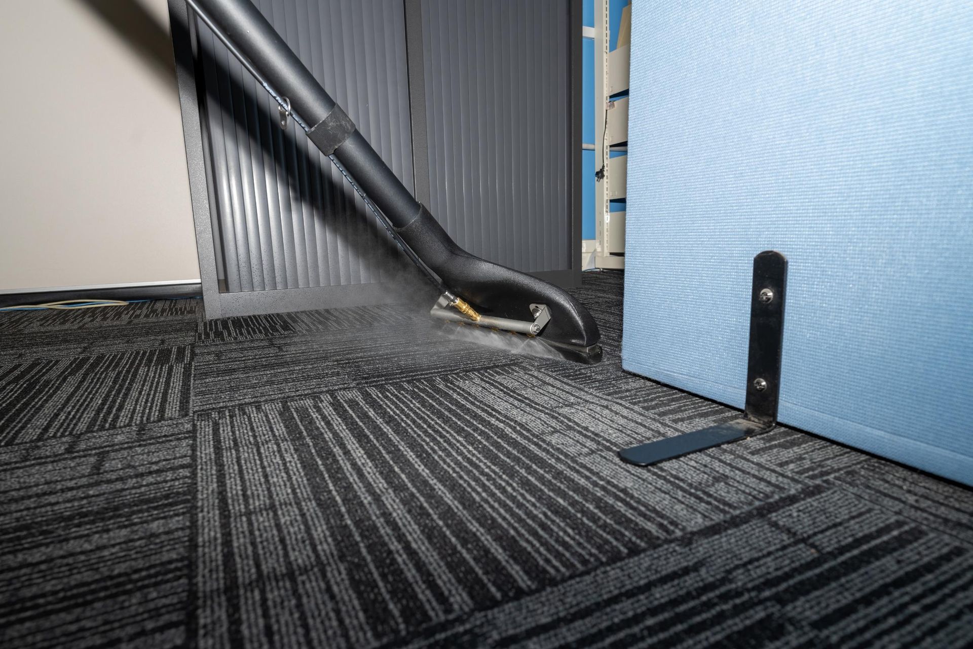 Vacuuming dark gray carpet near office dividers.