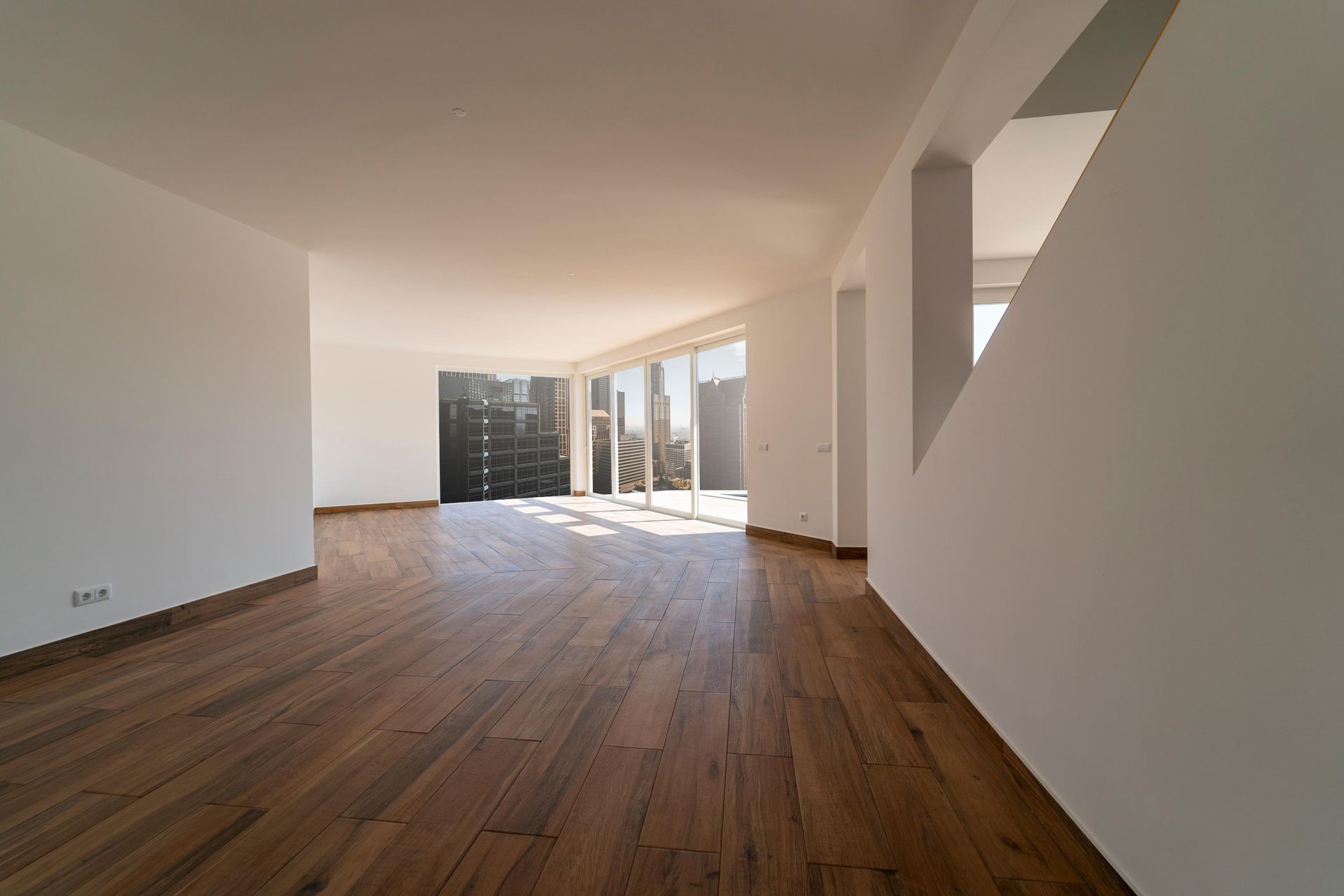 Empty room with hardwood floors, white walls, and large windows.