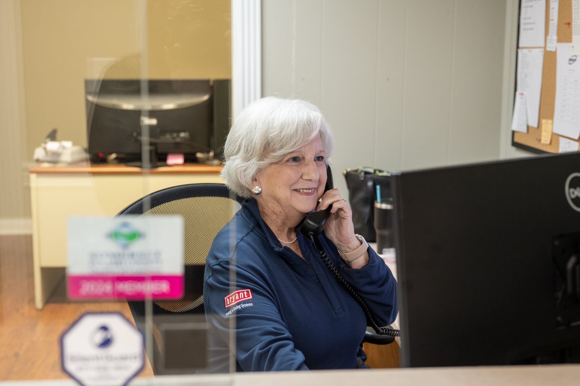 A woman is sitting at a desk talking on a cell phone in front of a computer.
