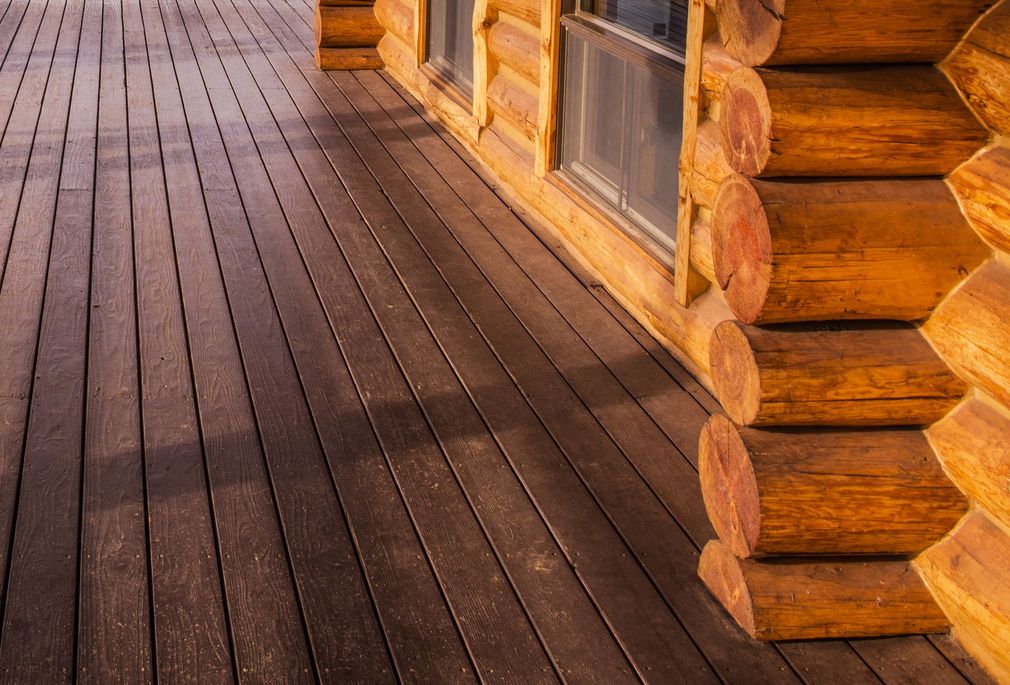 Wooden deck beside a log cabin wall and windows in warm sunlight