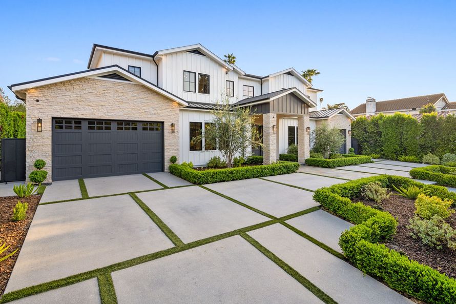 Modern suburban house with gray siding, green lawn, and a car parked in the driveway under a bright blue sky