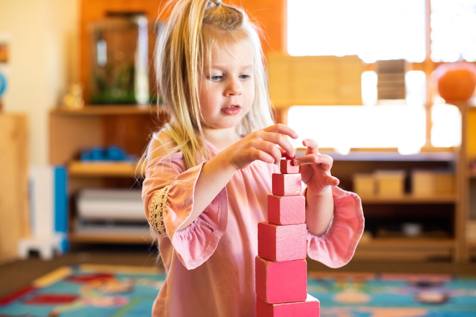 Child stacking pink blocks on a table in a bright classroom