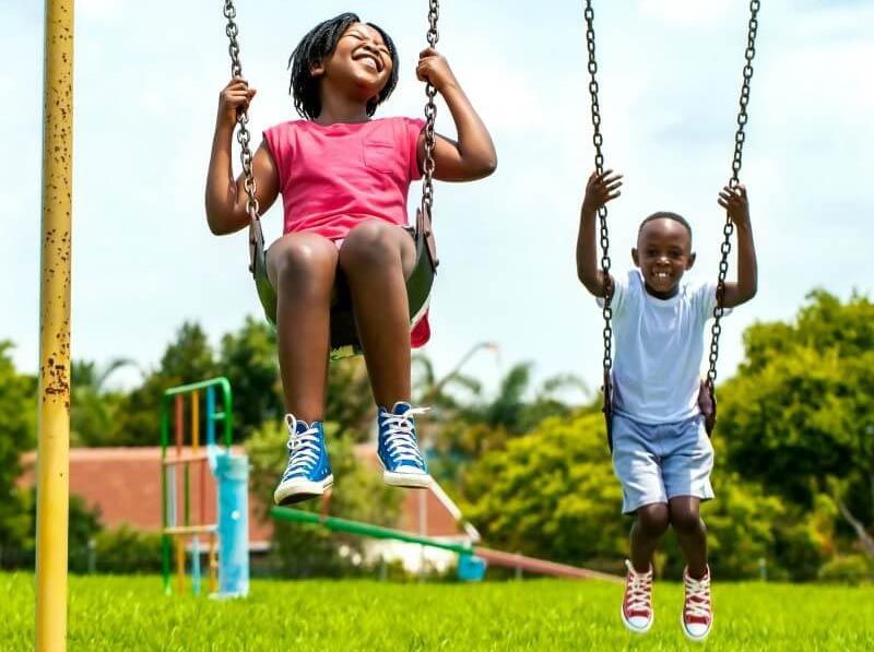A boy and a girl are playing on swings outdoor.