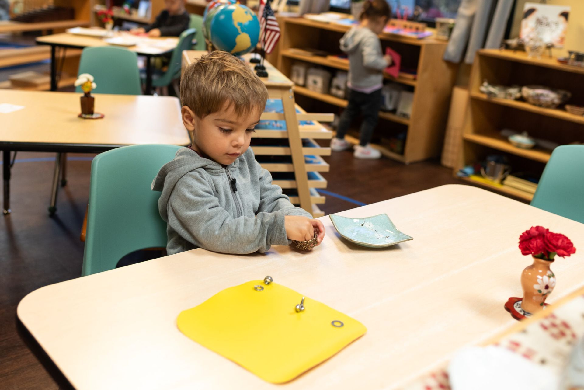 Montessori Toddler at a desk in a classroom, focused on activity.