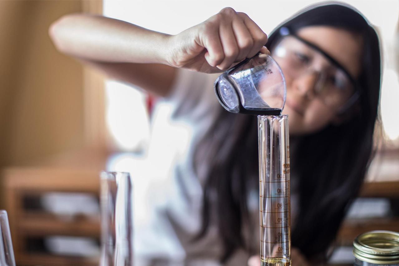 A Montessori student is pouring liquid into a beaker.