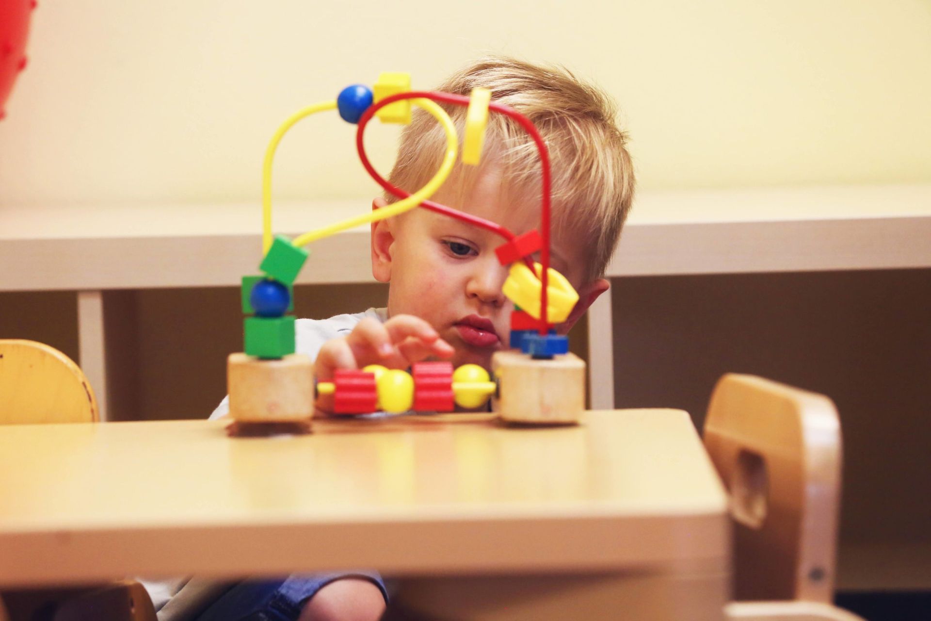 A Montessori infant is sitting at a table working with wooden bead maze