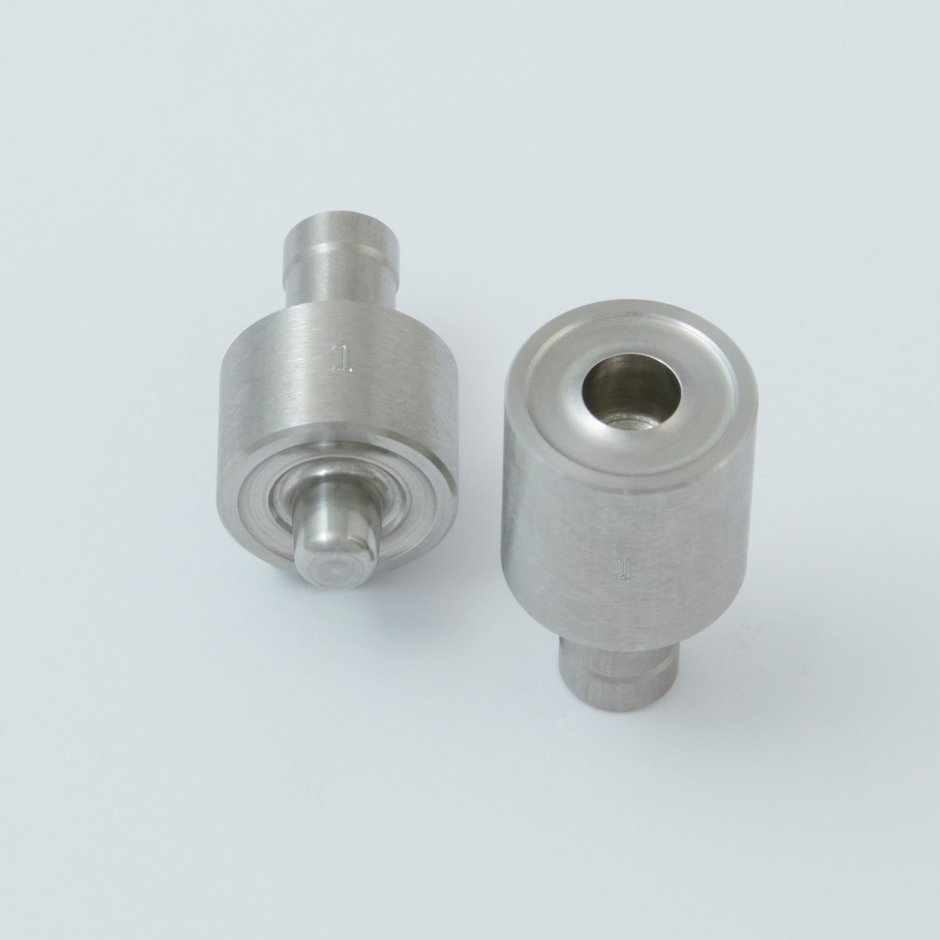 Two stainless steel tablet press punch and die components set against a plain light background.
