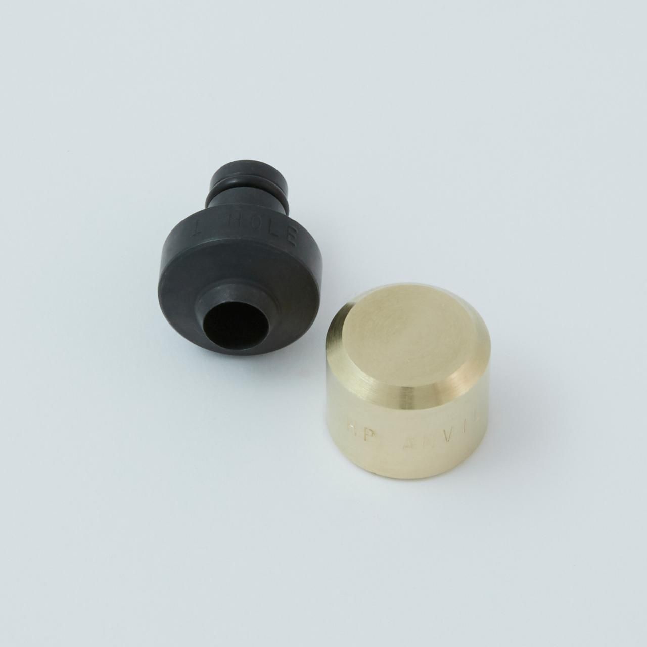 Two metal pieces on a white surface: a black, cylindrical object and a gold-colored, rounded piece.