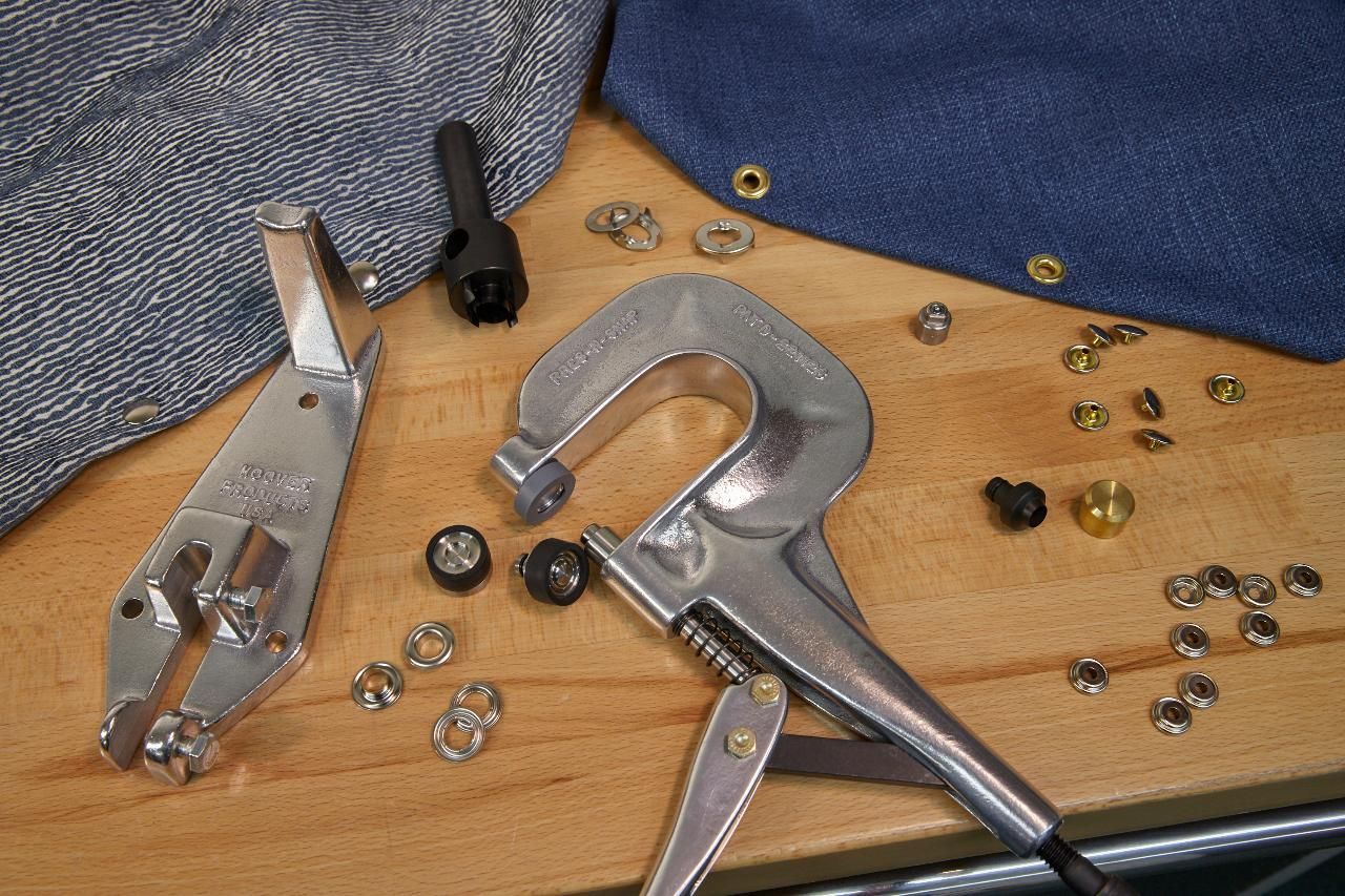 Tools and materials for setting grommets in fabric on wooden surface.