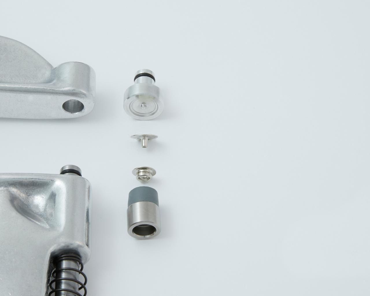 Disassembled metal snap press tool and components against a white backdrop.