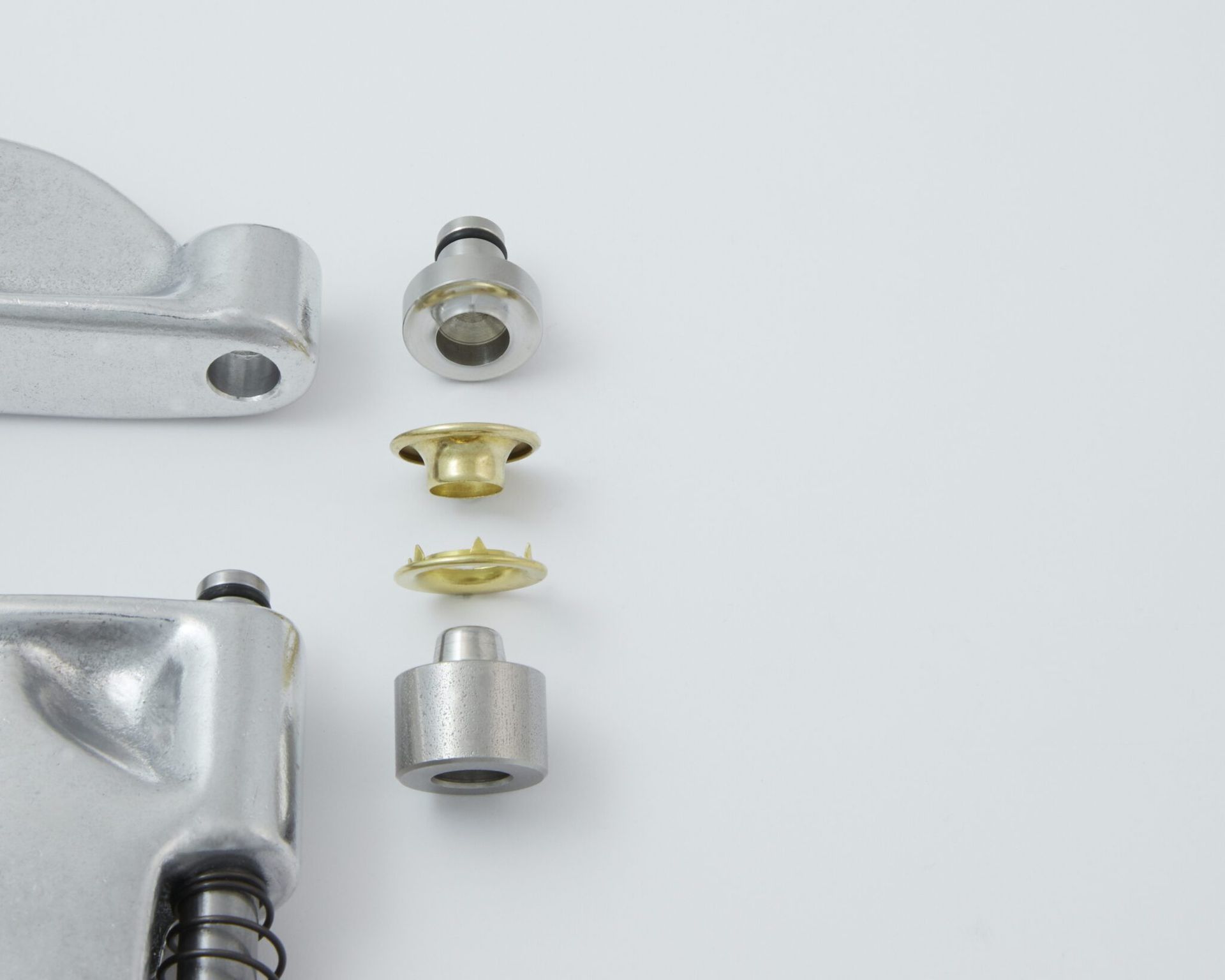 Metal rivet press with disassembled parts on a white surface.
