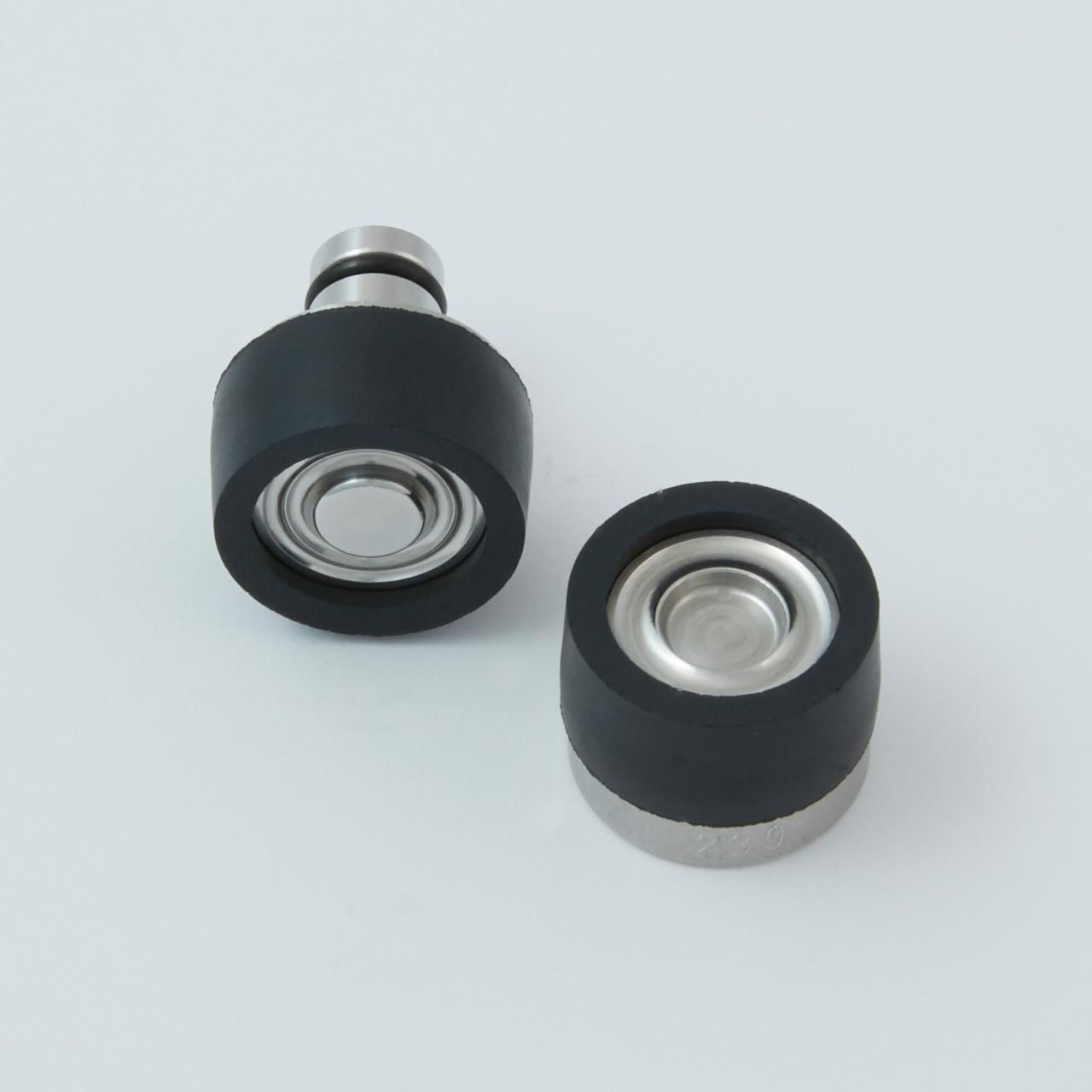 Two black and silver machine parts, cylindrical with protruding steel pieces, against a white background.