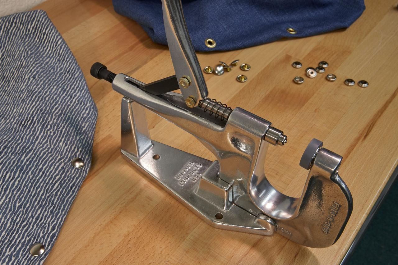 Metal eyelet press with leather and denim, wood table.