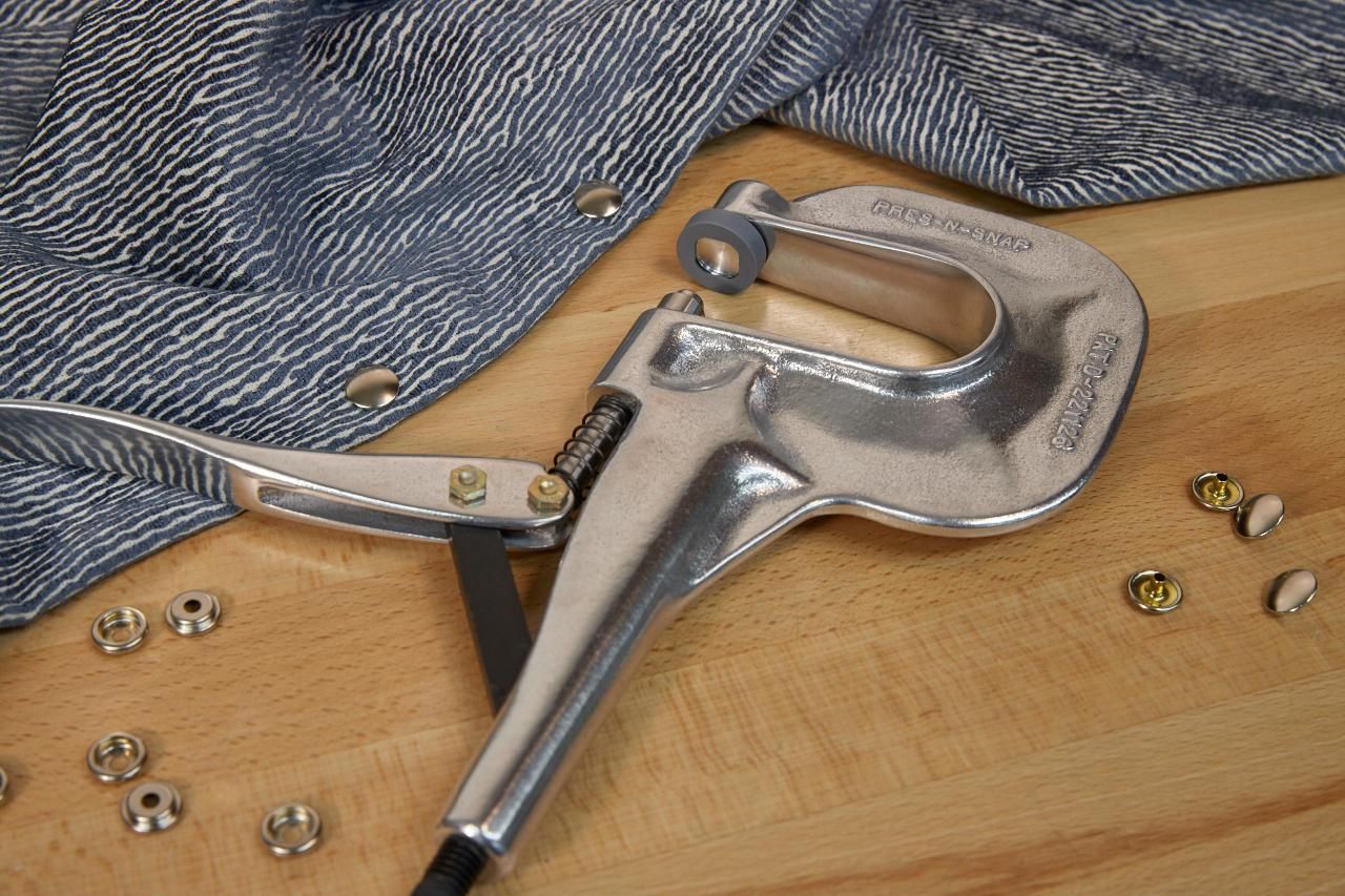 Metal grommet press with fabric, grommets, on wooden surface.