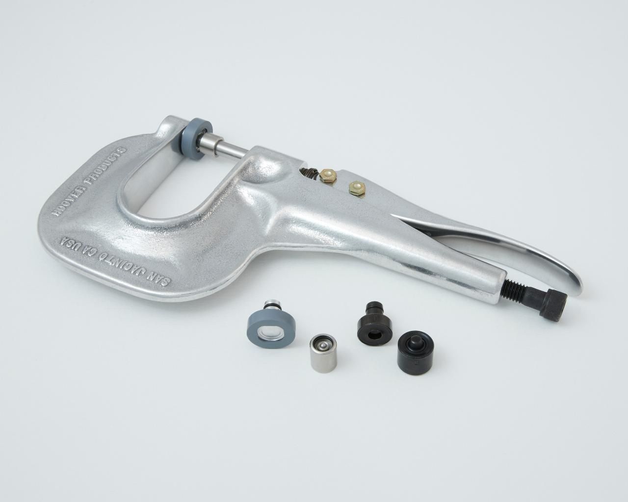 Silver rivet setting tool with interchangeable dies, lying on a white surface.