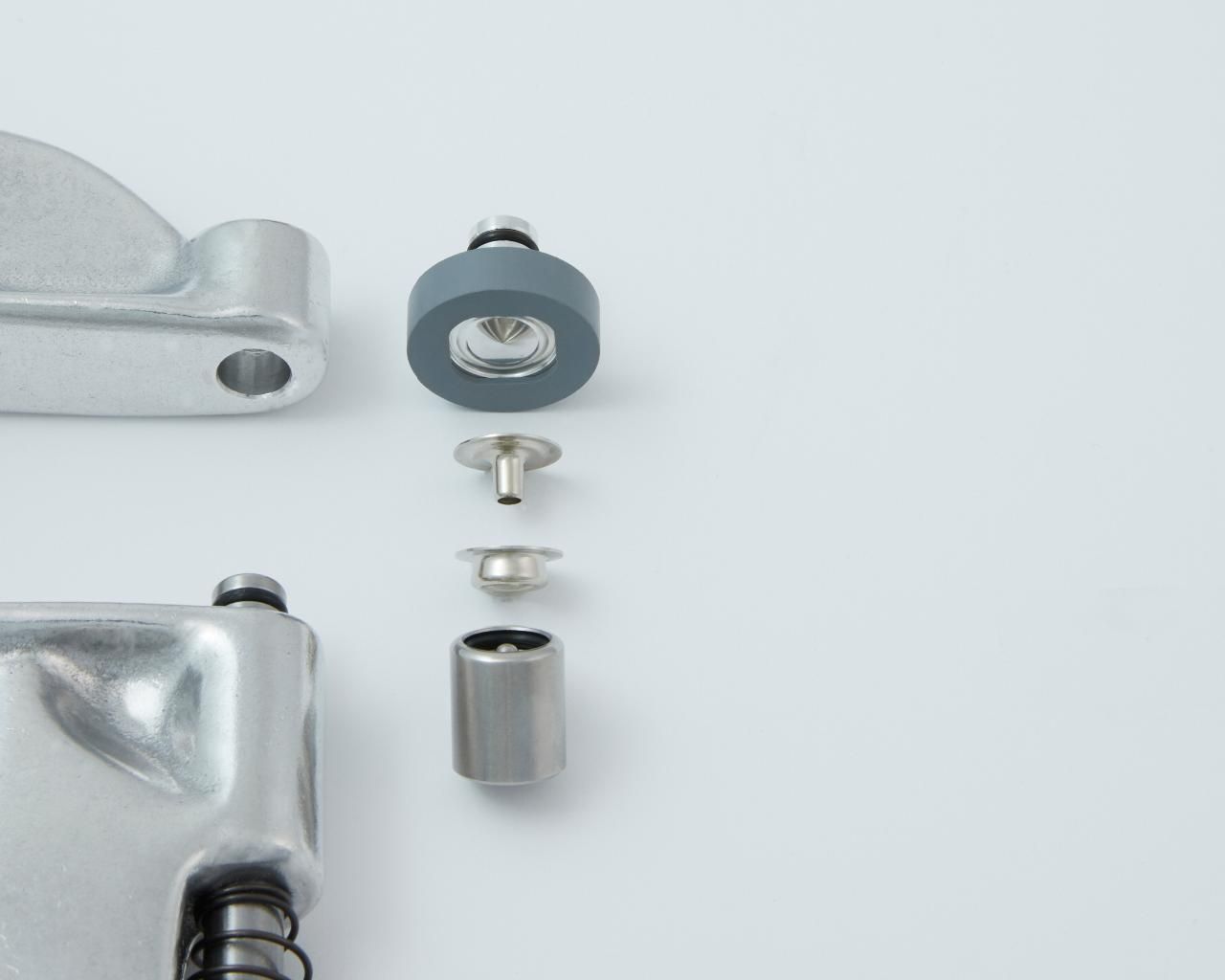 Exploded view of tool components: rubber washer, rivet, grommet, and metal cylindrical part, on a white surface.