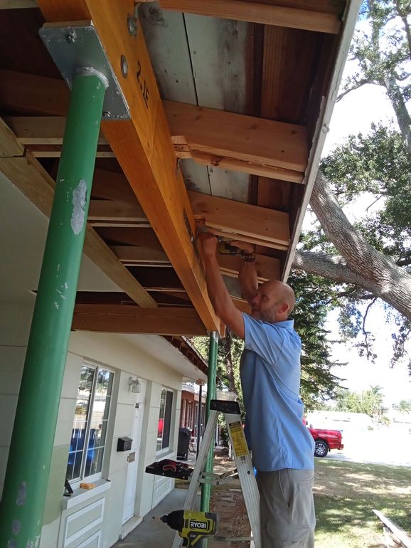 A man wearing a hard hat and plaid shirt is holding a tool belt