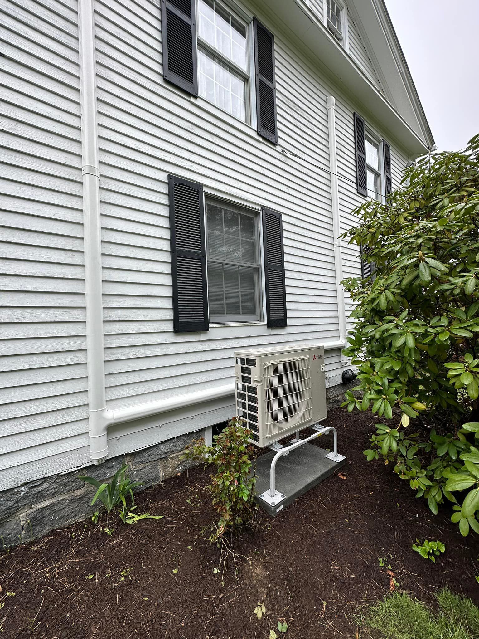 A white house with black shutters and a white air conditioner on the side of it.