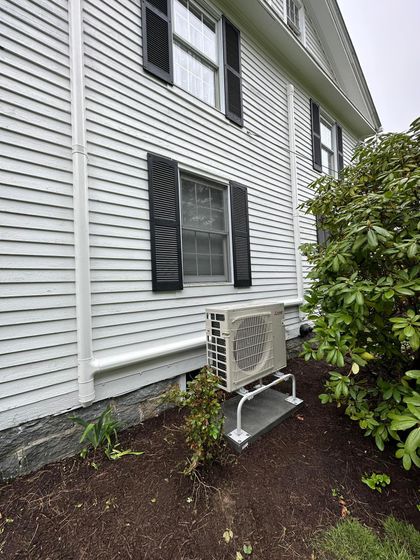 A white house with black shutters and a white air conditioner on the side of it.