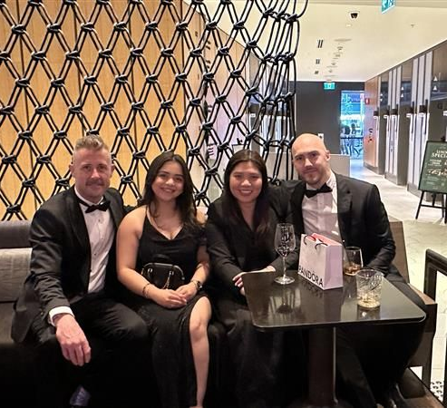 Four people in formal attire seated at a table. They are posing for a photo in a modern setting.
