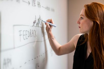Woman with red hair writing on a whiteboard labeled 