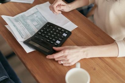 Woman’s hands on a calculator next to tax forms on a wooden desk. A coffee cup is visible.
