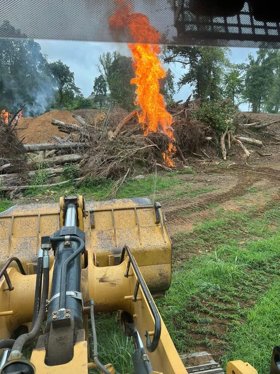 A bulldozer is cutting down trees in a field with a fire in the background.