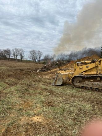 A bulldozer is moving dirt in a field with smoke coming out of it.