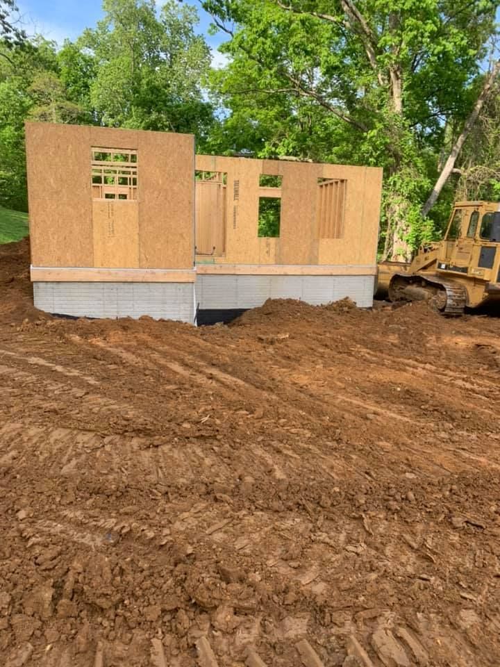 A house is being built in a dirt field with a bulldozer in the background.