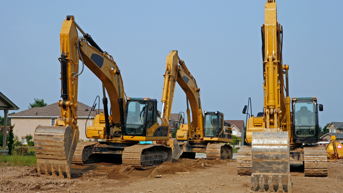 A row of yellow excavators are parked in a dirt field.